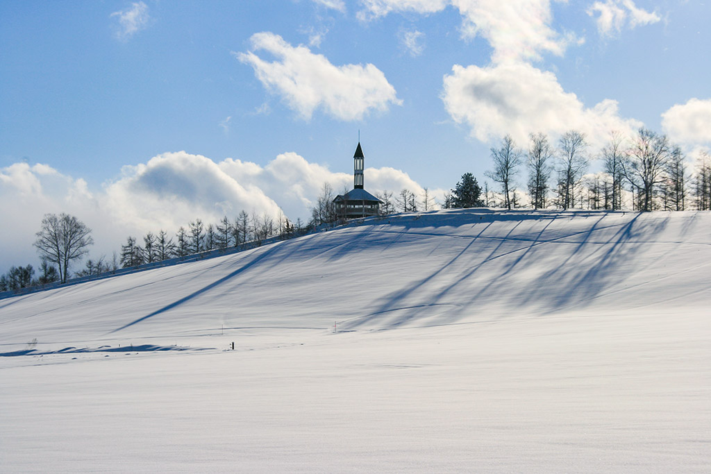 雪原が広がる冬の美瑛と丘の上に建つ塔のある美馬牛小学校